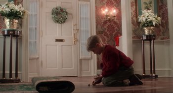 Movie still from “Home Alone” (1990), directed by Chris Columbus – A young boy sitting on the floor in front of a door; Wide shot, High angle
