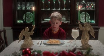 Movie still from “Home Alone” (1990), directed by Chris Columbus – A young boy sitting at a table with a plate of food; Medium shot, High angle