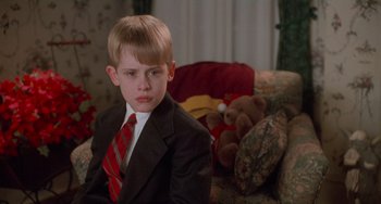 Movie still from “Home Alone 2: Lost in New York” (1992), directed by Chris Columbus – A boy in a suit and tie sitting in front of a teddy bear; Close Up shot, Low angle
