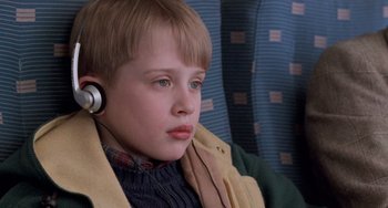 Movie still from “Home Alone 2: Lost in New York” (1992), directed by Chris Columbus – A young boy wearing a ear piece while sitting on a train; Close Up shot, Overhead angle