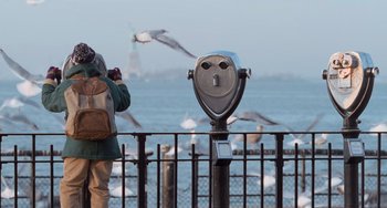 Movie still from “Home Alone 2: Lost in New York” (1992), directed by Chris Columbus – A man standing next to the ocean with seagulls flying in the background; Close Up shot, Low angle