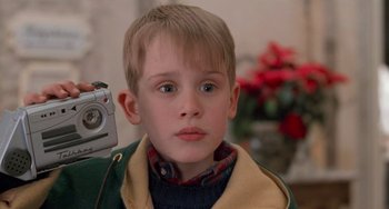 Movie still from “Home Alone 2: Lost in New York” (1992), directed by Chris Columbus – A young boy is holding a video camera in front of a mirror; Close Up shot, Low angle