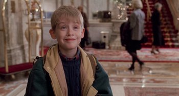 Movie still from “Home Alone 2: Lost in New York” (1992), directed by Chris Columbus – A young boy smiling for the camera while standing in a room; Medium shot, Low angle