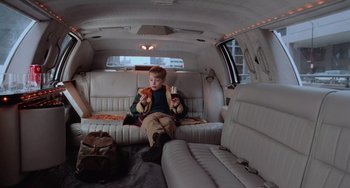 Movie still from “Home Alone 2: Lost in New York” (1992), directed by Chris Columbus – A boy sitting in the back of a car eating pizza; Wide shot, High angle
