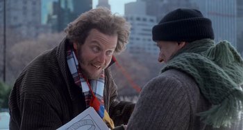 Movie still from “Home Alone 2: Lost in New York” (1992), directed by Chris Columbus – A man in a scarf is holding a book and talking to another man in a scarf; Medium shot, Over the shoulder angle