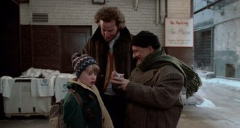 Movie still from “Home Alone 2: Lost in New York” (1992), directed by Chris Columbus – Two men and a boy looking at a cell phone; Medium shot, Over the shoulder angle