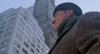 Movie still from “Home Alone 2: Lost in New York” (1992), directed by Chris Columbus – A man wearing a hat and a scarf standing in front of a tall building; Close Up shot, Low angle