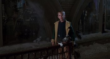 Movie still from “Home Alone 2: Lost in New York” (1992), directed by Chris Columbus – A young boy standing next to a fence with pigeons; Wide shot, Low angle