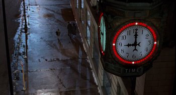 Movie still from “Home Alone 2: Lost in New York” (1992), directed by Chris Columbus – A clock on the side of a building lit up at night; Extreme Wide shot, Overhead angle
