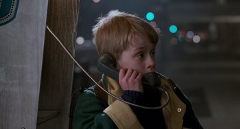Movie still from “Home Alone 2: Lost in New York” (1992), directed by Chris Columbus – A young boy talking on a phone while standing next to a tree; Close Up shot, Low angle