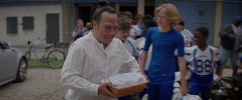 Movie still from “Home Team” (2022), directed by Charles Kinnane – A man holding a basket of food in front of a group of people; Medium shot, Over the shoulder angle