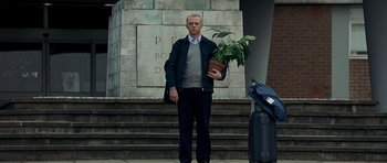 Movie still from “Hot Fuzz” (2007), directed by Edgar Wright – A man holding a potted plant on the steps of a building; Wide shot, Low angle