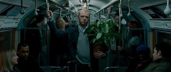 Movie still from “Hot Fuzz” (2007), directed by Edgar Wright – A man holding a potted plant on a crowded bus; Medium shot, Over the shoulder angle