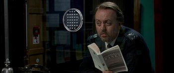 Movie still from “Hot Fuzz” (2007), directed by Edgar Wright – A man reading a book in front of a window; Close Up shot, Over the shoulder angle