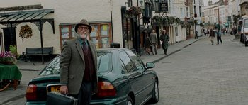 Movie still from “Hot Fuzz” (2007), directed by Edgar Wright – An older man standing next to a car on a city street; Wide shot, Over the shoulder angle
