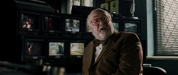 Movie still from “Hot Fuzz” (2007), directed by Edgar Wright – An older man in a suit and bow tie in front of a bunch of tv monitors; Close Up shot, Over the shoulder angle