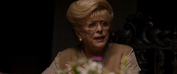 Movie still from “Hot Fuzz” (2007), directed by Edgar Wright – An older woman wearing glasses and a necklace; Close Up shot, Over the shoulder angle