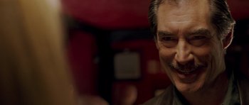 Movie still from “Hot Fuzz” (2007), directed by Edgar Wright – An older man smiling for the camera in front of a red wall; Close Up shot, Over the shoulder angle
