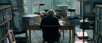 Movie still from “Hot Fuzz” (2007), directed by Edgar Wright – A man sitting at a desk in front of stacks of papers; Wide shot, High angle