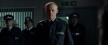 Movie still from “Hot Fuzz” (2007), directed by Edgar Wright – A man in a police uniform standing in front of two other men; Medium shot, Low angle