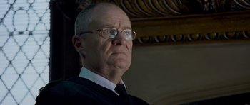 Movie still from “Hot Fuzz” (2007), directed by Edgar Wright – An older man wearing glasses and a black tie; Close Up shot, Low angle