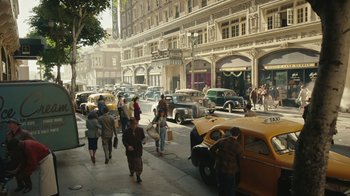 Movie still from “A League of Their Own” (2022), created by Abbi Jacobson – A group of people walking down a street near parked cars; Extreme Wide shot, High angle