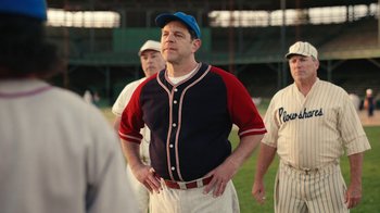 Movie still from “A League of Their Own” (2022), created by Abbi Jacobson – A man in a baseball uniform standing on a baseball field; Medium shot, Over the shoulder angle