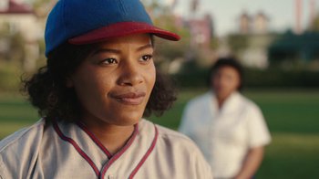 Movie still from “A League of Their Own” (2022), created by Abbi Jacobson – A woman wearing a baseball uniform and a red and blue hat; Close Up shot, Over the shoulder angle