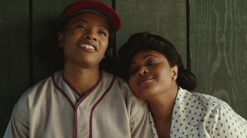 Movie still from “A League of Their Own” (2022), created by Abbi Jacobson – A man and a woman sitting next to each other; Close Up shot, Overhead angle
