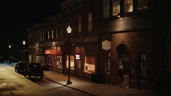 Movie still from “A League of Their Own” (2022), created by Abbi Jacobson – A person standing on the sidewalk in front of a store; Extreme Wide shot, High angle
