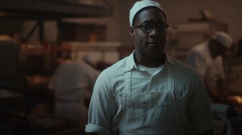 Movie still from “A League of Their Own” (2022), created by Abbi Jacobson – A man in a white apron and a white hat; Close Up shot, Over the shoulder angle