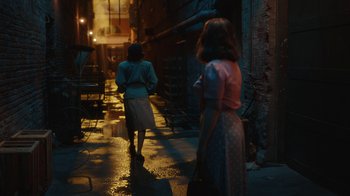 Movie still from “A League of Their Own” (2022), created by Abbi Jacobson – Two women walking down a wet street at night; Wide shot, Over the shoulder angle