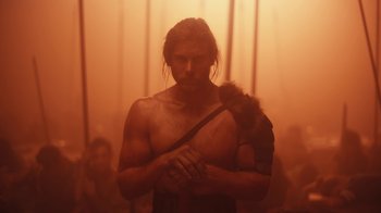 Movie still from “Euphoria” (2019), created by Sam Levinson – A man with long hair and a bare torso holding a monkey; Medium shot, Low angle