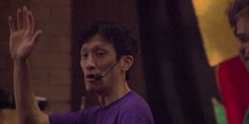 Movie still from “Hot Potato: The Story of the Wiggles” (2023), directed by Fraser Grut – A man wearing a purple t - shirt is talking on a microphone; Close Up shot, Low angle