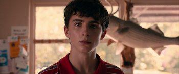 Movie still from “Hot Summer Nights” (2017), directed by Elijah Bynum – A young man in a red shirt is looking at the camera; Close Up shot, Over the shoulder angle