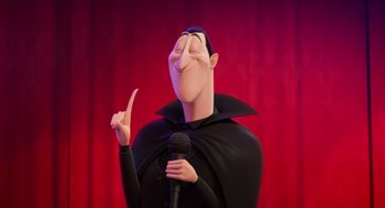 Movie still from “Hotel Transylvania 4: Transformania” (2022), directed by Jennifer Kluska – A cartoon of a man in a black robe holding a microphone; Medium shot, Low angle