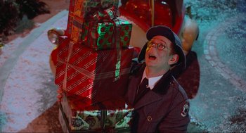 Movie still from “How the Grinch Stole Christmas” (2000), directed by Ron Howard – A man in a hat and glasses holding a stack of christmas presents; Close Up shot, Overhead angle