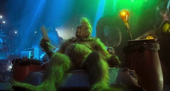 Movie still from “How the Grinch Stole Christmas” (2000), directed by Ron Howard – A person dressed as the grinch sitting in a chair holding a paper; Medium shot, Low angle