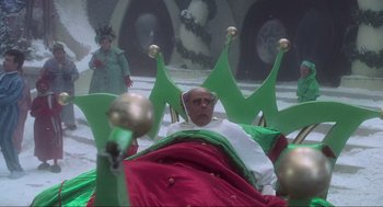 Movie still from “How the Grinch Stole Christmas” (2000), directed by Ron Howard – A man sitting in a chair wearing a green hat; Wide shot, High angle