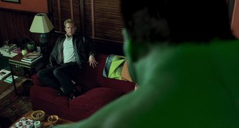 Movie still from “Hulk” (2003), directed by Ang Lee – A man sitting on top of a red couch next to another man; Medium shot, Over the shoulder angle