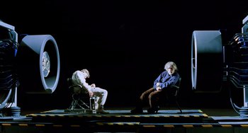 Movie still from “Hulk” (2003), directed by Ang Lee – Two people sitting on a stage with one sitting on a chair; Wide shot, High angle