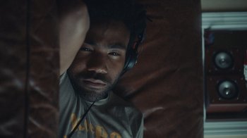 Movie still from “Atlanta” (2016), created by Donald Glover – A man with headphones is sitting on a couch; Close Up shot, Overhead angle