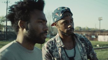Movie still from “Atlanta” (2016), created by Donald Glover – Two black men standing next to each other in a field; Close Up shot, Over the shoulder angle