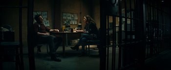 Movie still from “Hypnotic” (2023), directed by Robert Rodriguez – A woman sitting at a table in a dark room; Wide shot, High angle