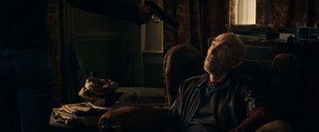 Movie still from “Hypnotic” (2023), directed by Robert Rodriguez – A man sitting in a chair holding a remote control; Medium shot, Over the shoulder angle