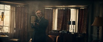 Movie still from “Hypnotic” (2023), directed by Robert Rodriguez – A man standing in a living room holding a remote control; Medium shot, Low angle