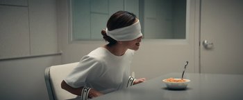 Movie still from “Hypnotic” (2023), directed by Robert Rodriguez – A blindfolded woman sitting in front of a bowl of food; Medium shot, Over the shoulder angle