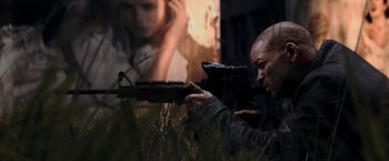 Movie still from “I Am Legend” (2007), directed by Francis Lawrence – A man is holding a rifle in the grass; Medium shot, Over the shoulder angle