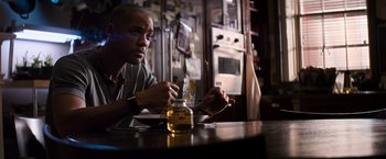 Movie still from “I Am Legend” (2007), directed by Francis Lawrence – A man sitting at a table in front of a jar; Medium shot, Over the shoulder angle