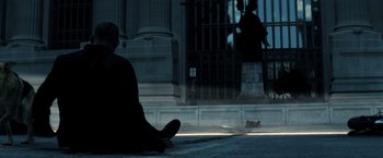Movie still from “I Am Legend” (2007), directed by Francis Lawrence – A person sitting on the ground in front of a building; Wide shot, Low angle